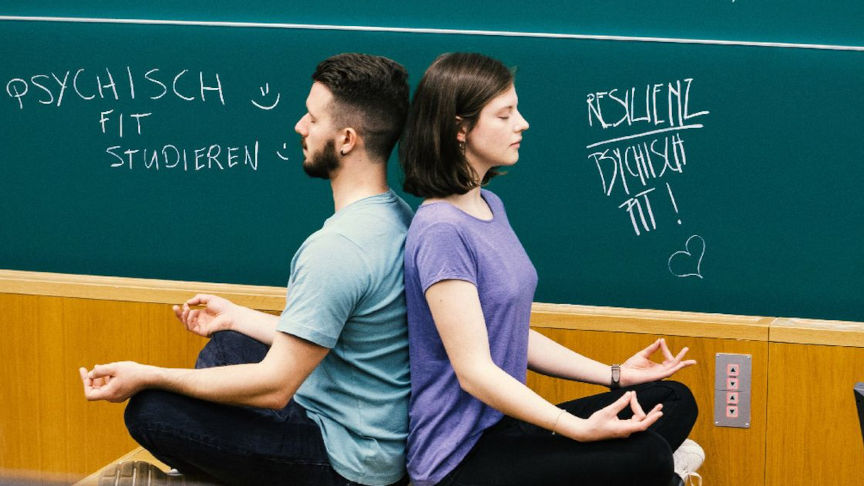 Foto von einem Studenten und einer Studentin bei Meditationsübung im Hörsaal