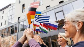 Hochschulmitarbeitende halten kleine Fahnen europäischer Länder in die Luft